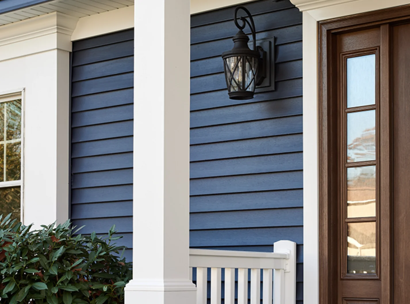 Blue horizontal siding with white porch trim beside a wood entry door